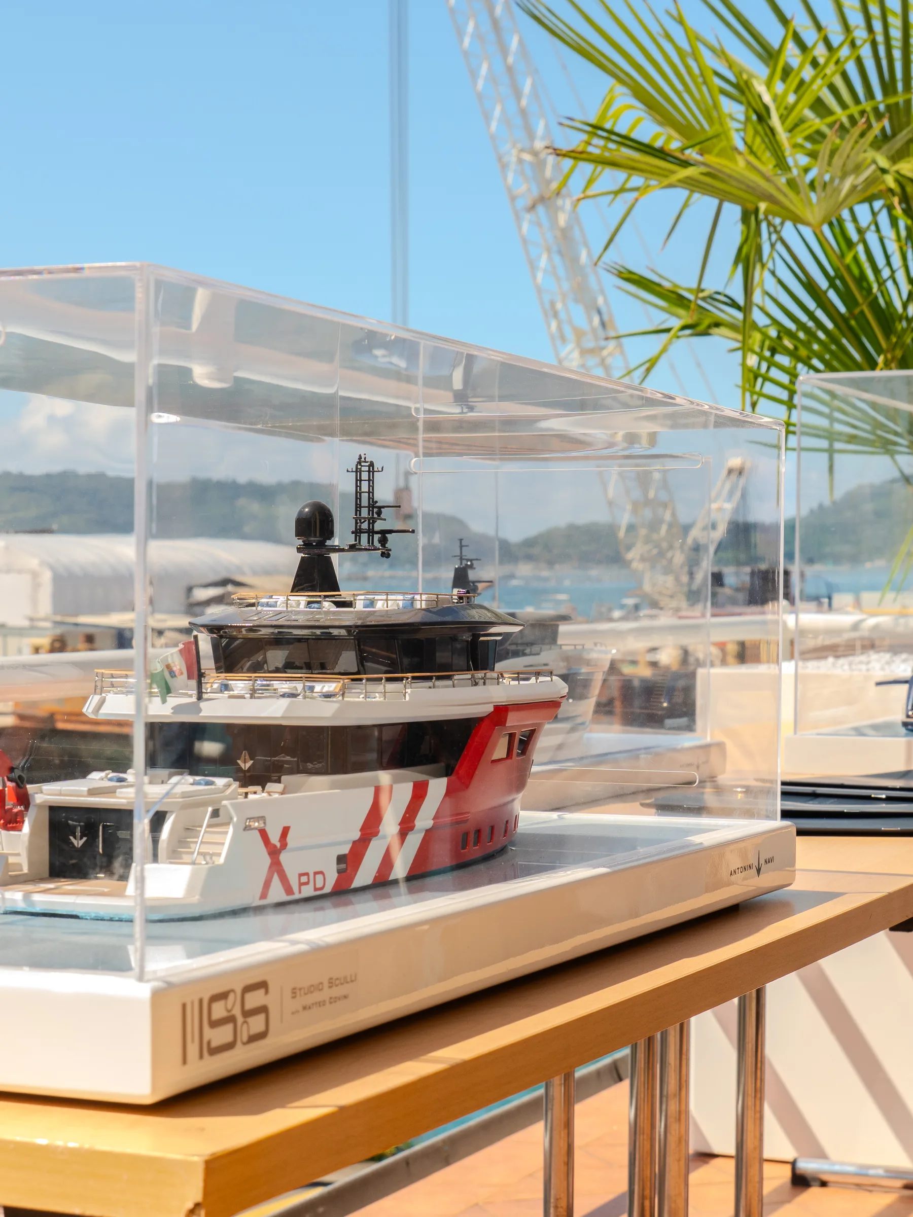 Modelli di navi in teche di vetro esposti in banchina al cantiere Antonini Navi, con lo scafo di uno yacht sullo sfondo