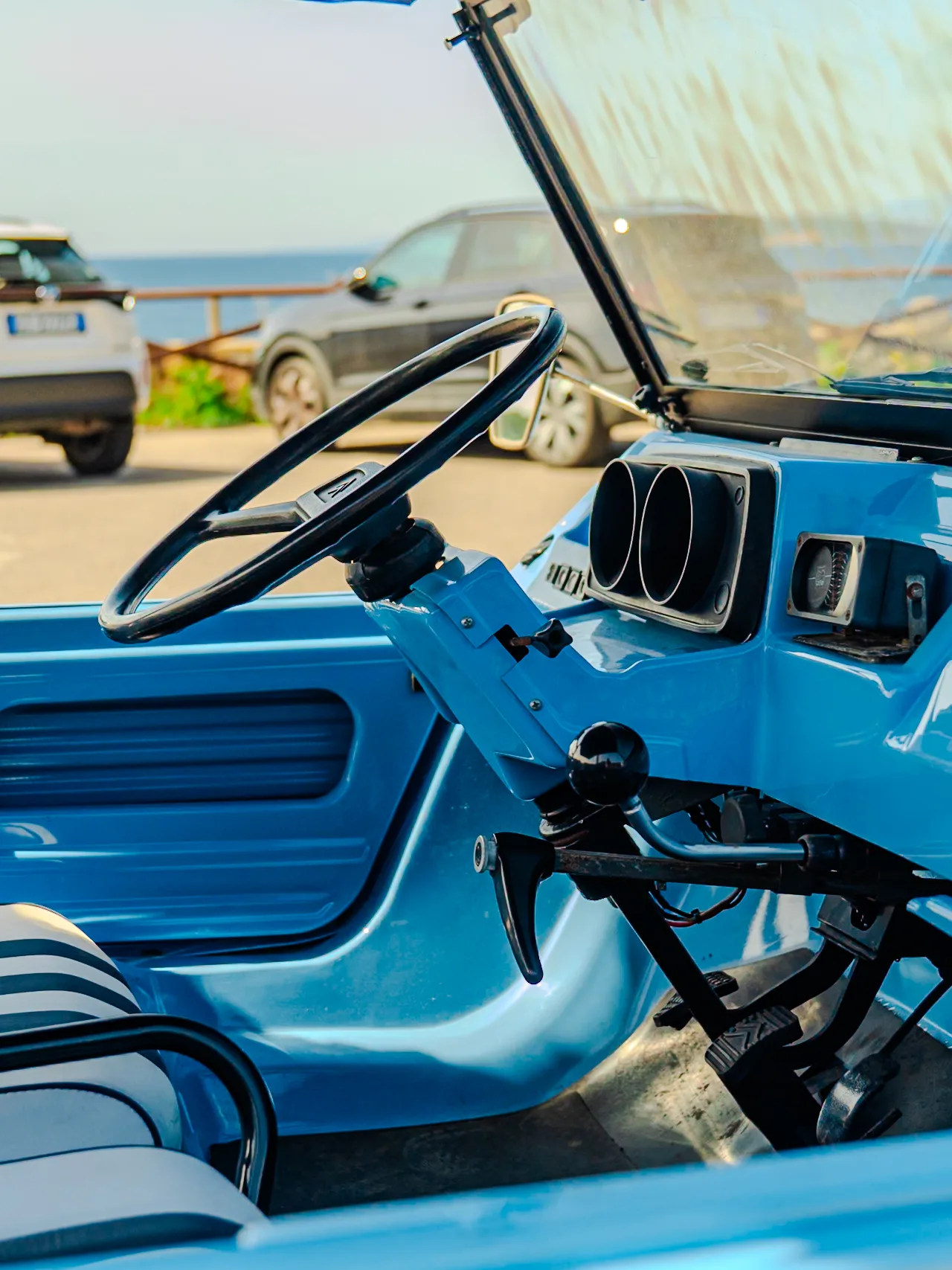 Interno di una spiaggina blu parcheggiata davanti al mare alla Maddalena, col volante in primo piano