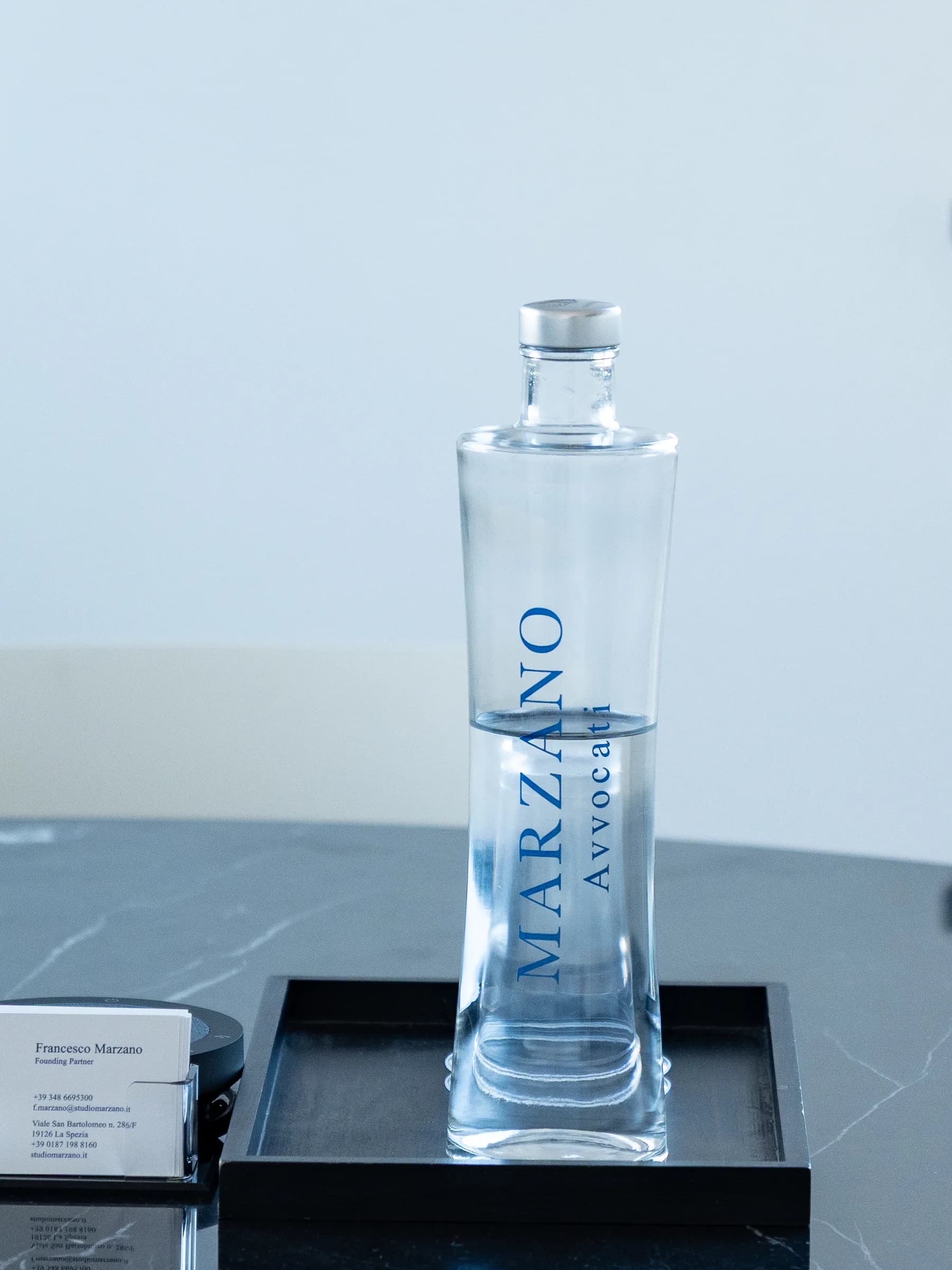 Bottiglia d'acqua personalizzata Marzano Avvocati sul tavolo di marmo nero, accanto al portabiglietti