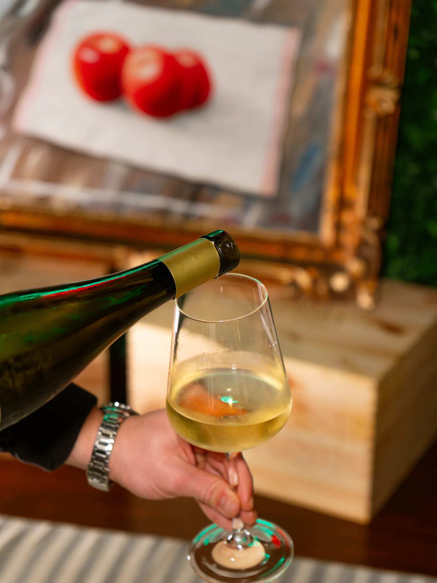 Vino bianco versato in un calice al tavolo del Pin Bon, con una cornice dorata sullo sfondo