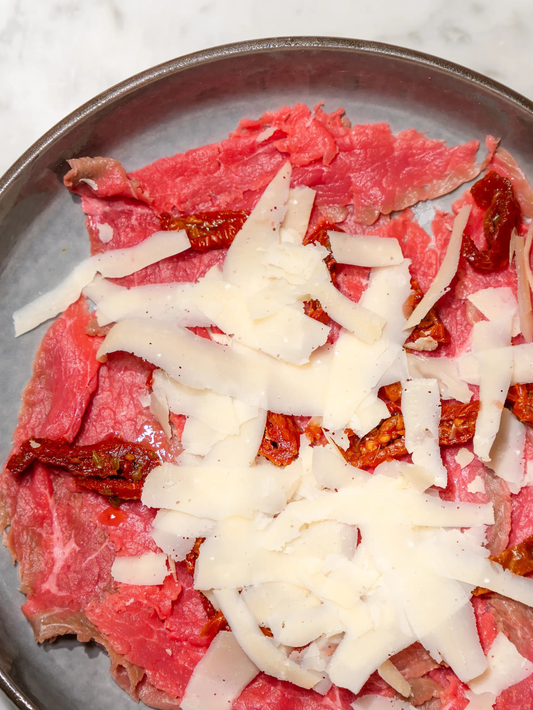 Carpaccio di manzo con scaglie di formaggio e pomodori secchi, servito al Pin Bon