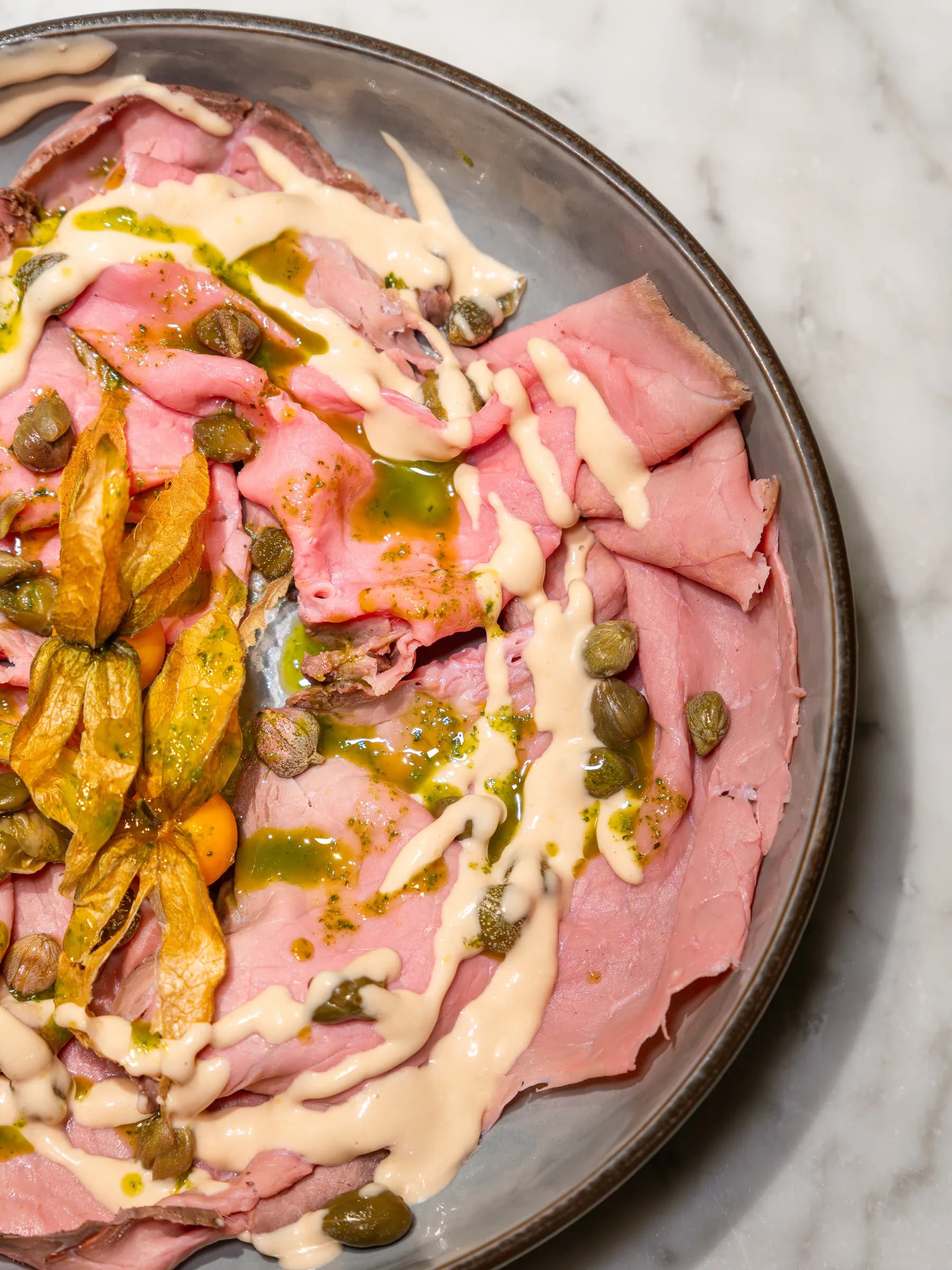 Fettine di carne rosata con salsa tonnata, capperi e fiori di zucca, servite al Pin Bon