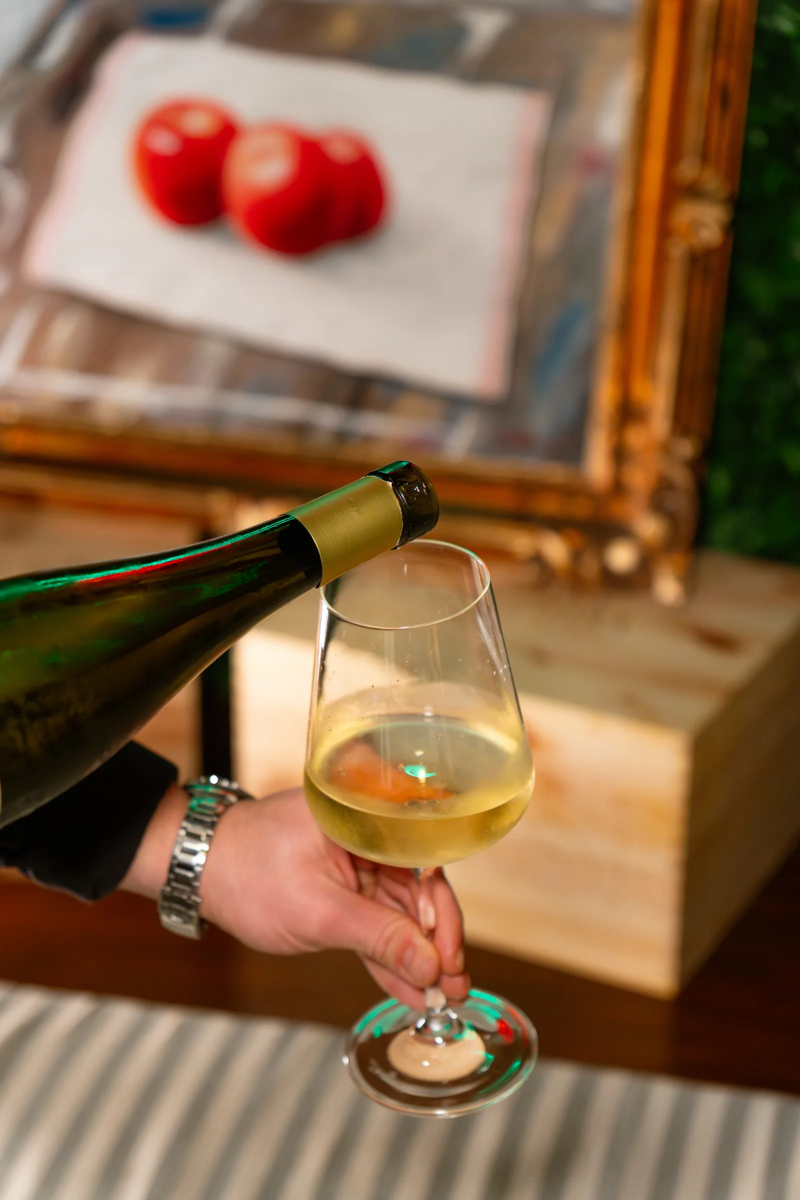 Vino bianco versato in un calice al tavolo del Pin Bon, con una cornice dorata sullo sfondo