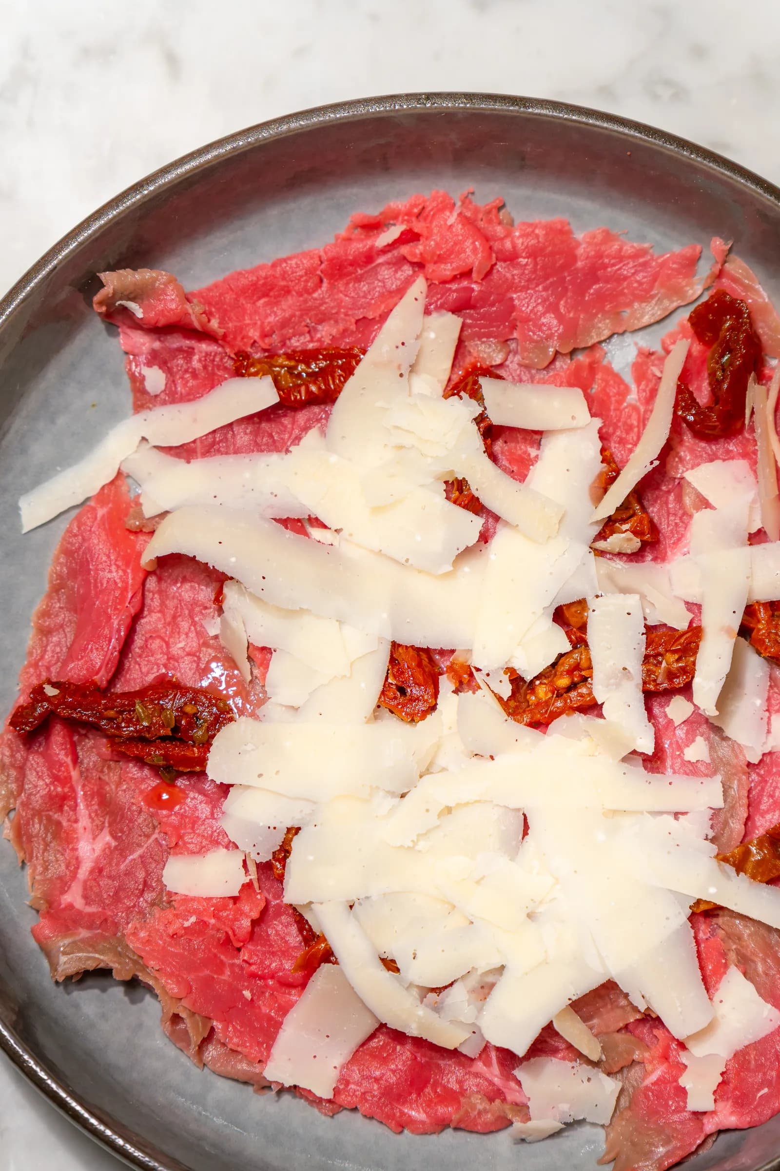 Carpaccio di manzo con scaglie di formaggio e pomodori secchi, servito al Pin Bon