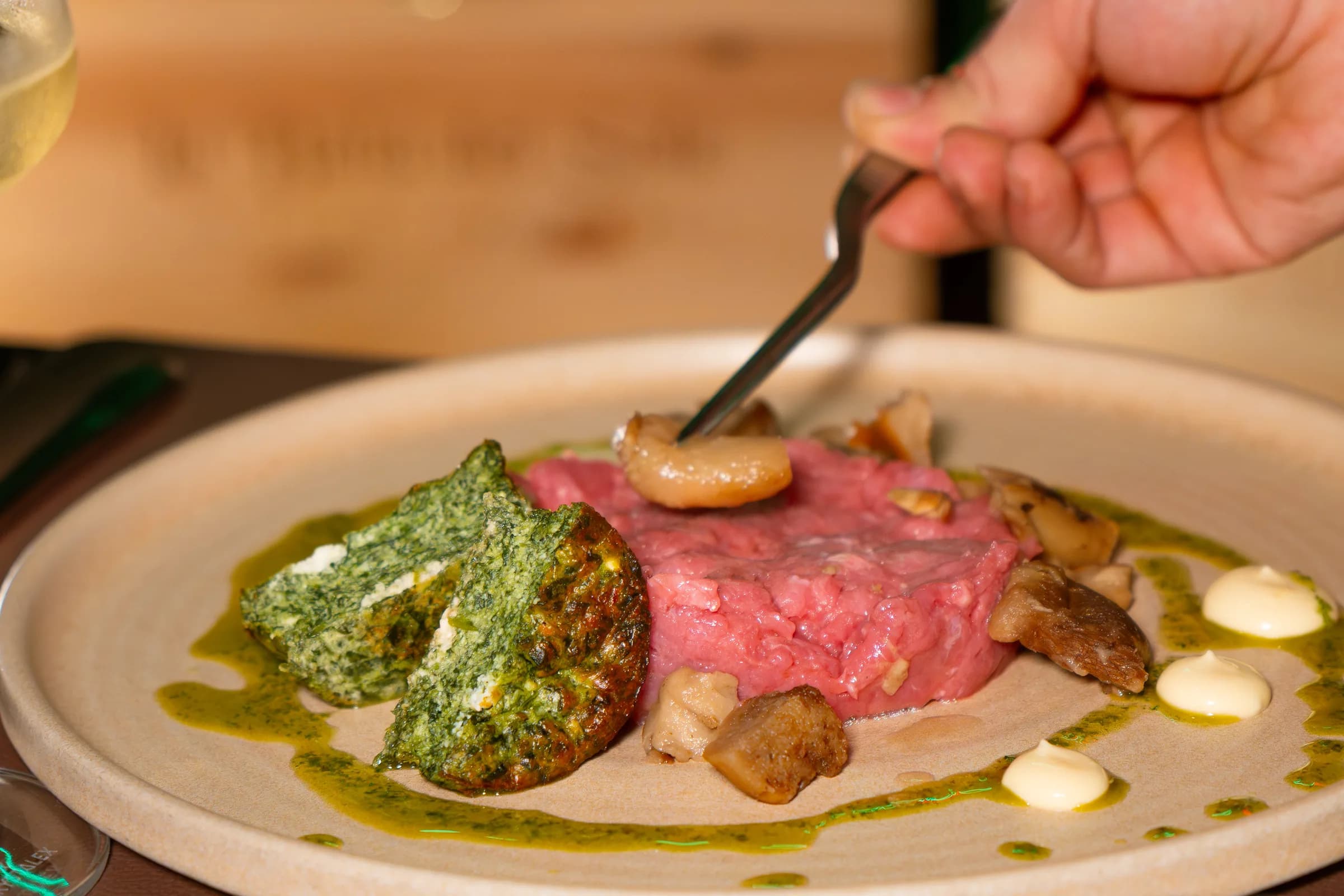 Mano con la forchetta su una tartare di manzo con salsa alle erbe e funghi, servita al tavolo del Pin Bon