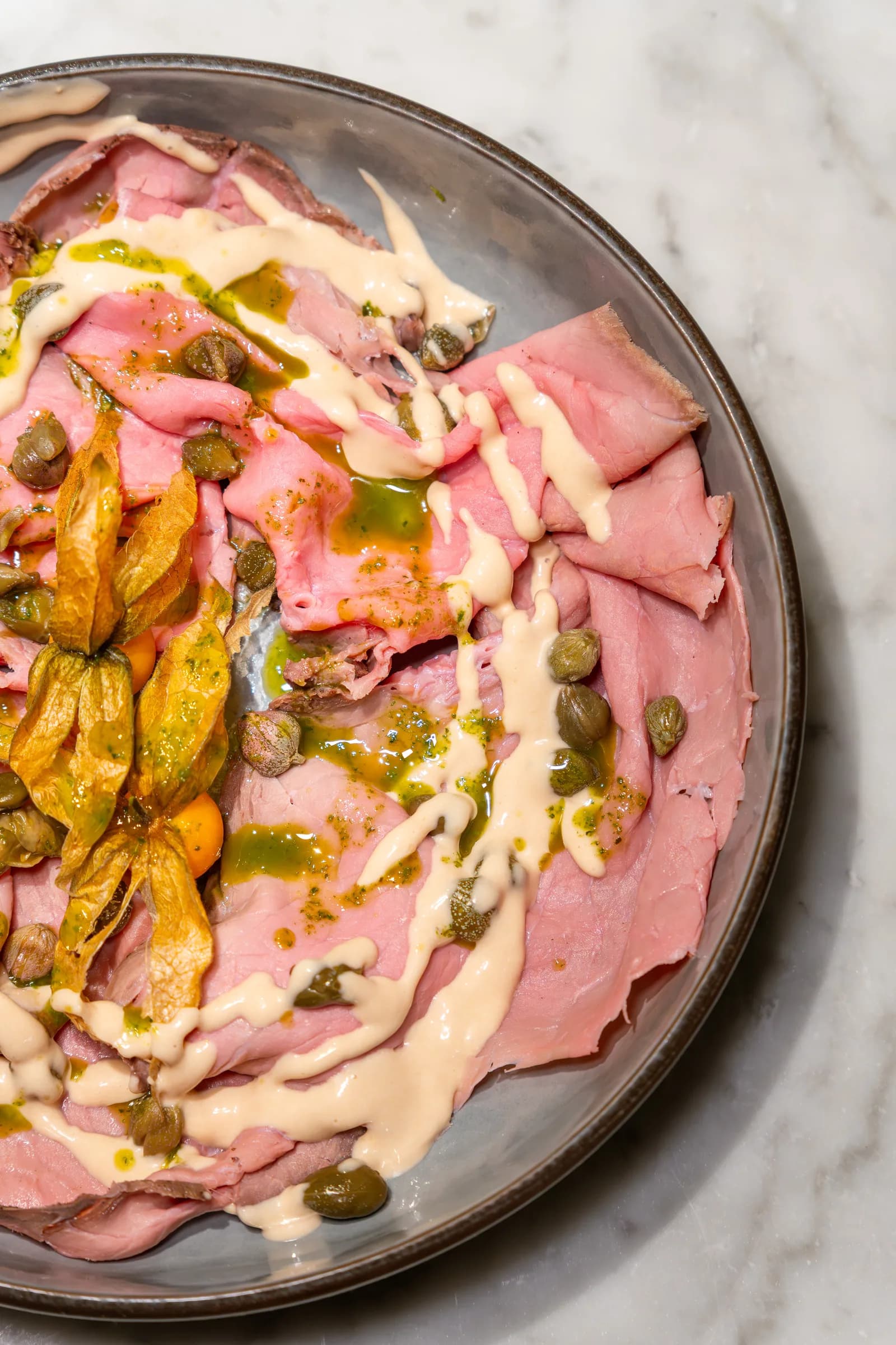Fettine di carne rosata con salsa tonnata, capperi e fiori di zucca, servite al Pin Bon