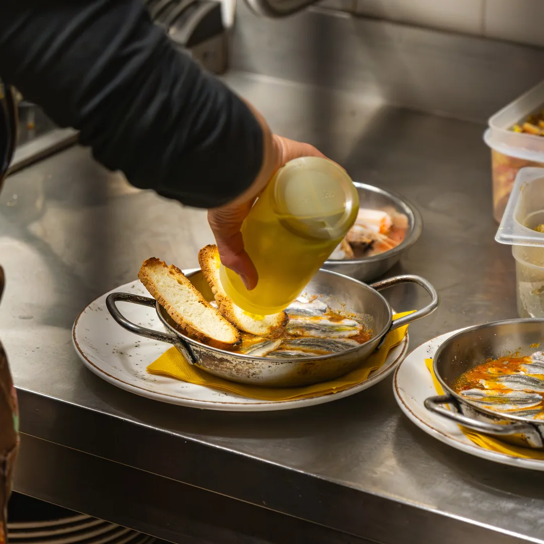 Olio versato a filo su un piatto di crostini, in cucina durante il servizio