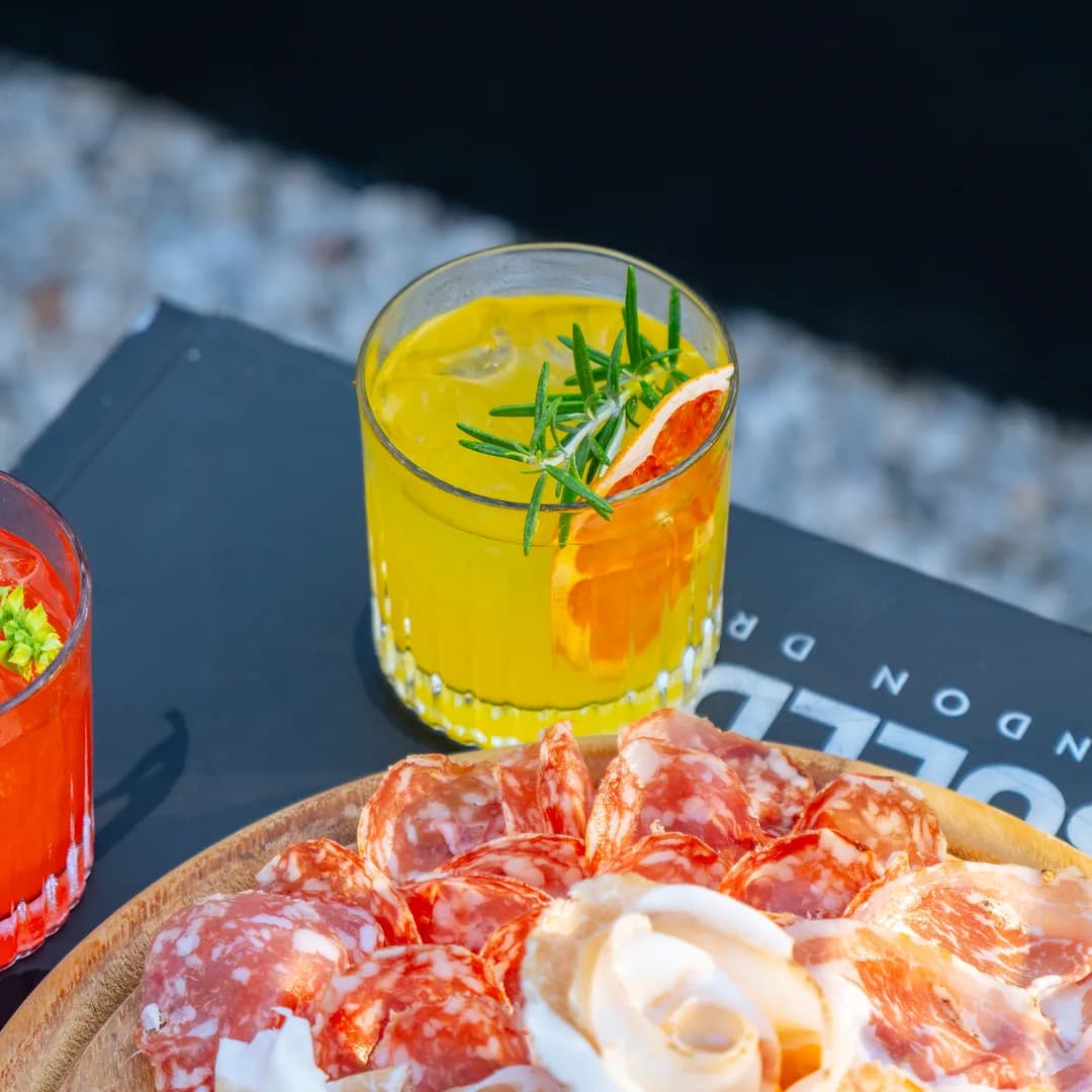 Cocktail giallo con rosmarino e tagliere di salumi ripresi dall'alto