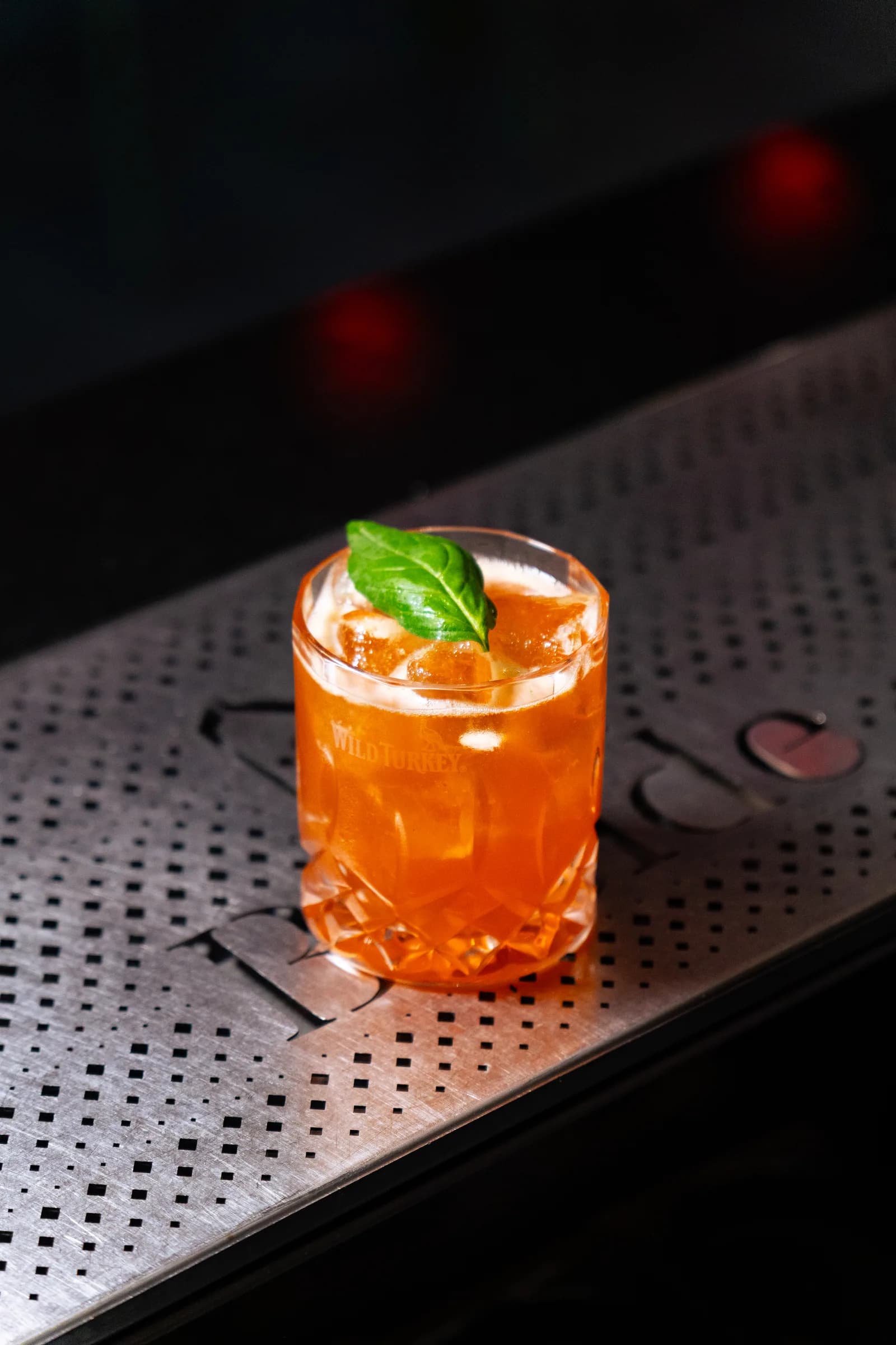 Cocktail arancione con foglia di basilico sul bancone in acciaio del PiN la Spezia