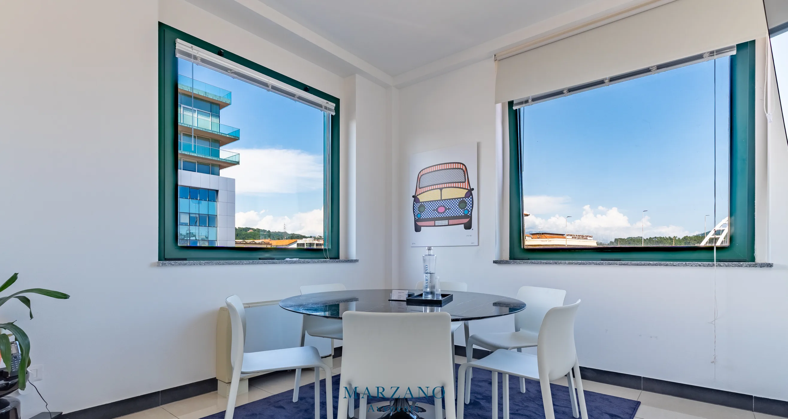 La sala riunioni dello studio Marzano con due grandi finestre sul golfo, il tavolo rotondo e la stampa alla parete