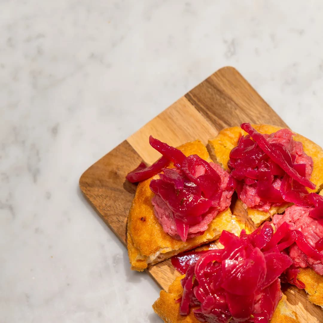 Bruschette di focaccia con cipolla rossa e carne cruda sul tagliere