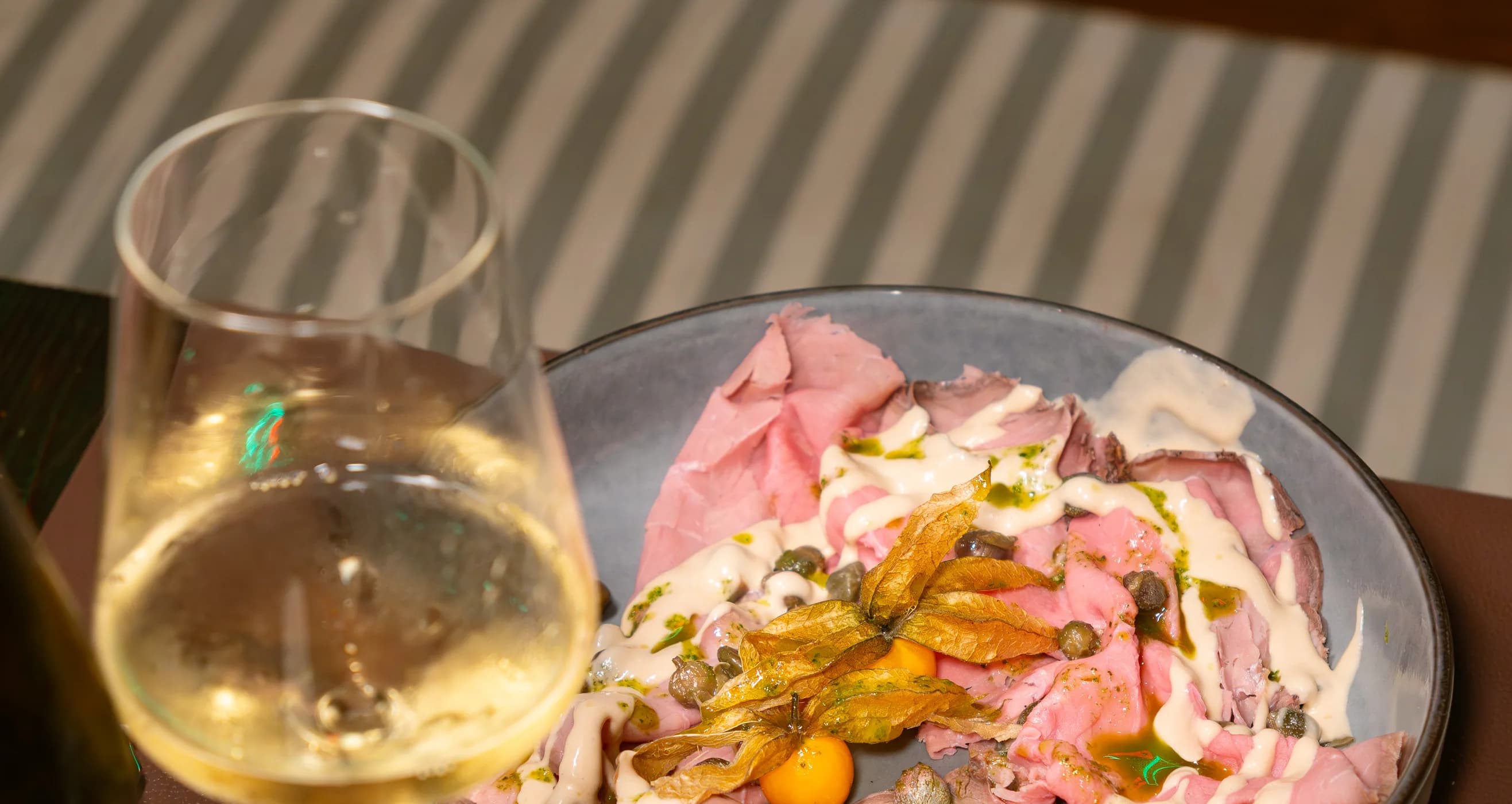 Il vitello tonnato servito nel piatto accanto a un calice di bianco, sul tavolo del bistrot