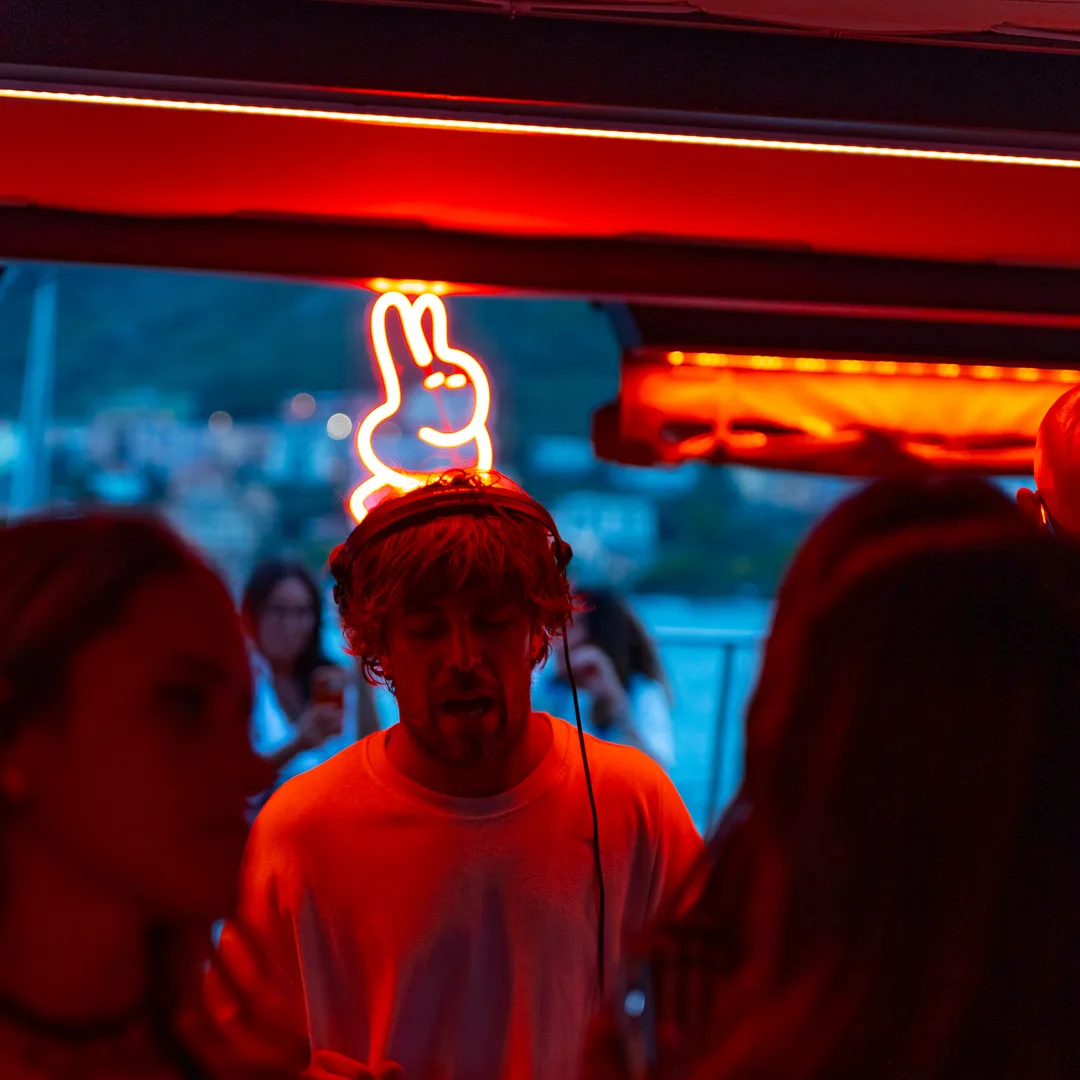 Il dj in consolle sotto l'insegna al neon, nella luce rossa del locale