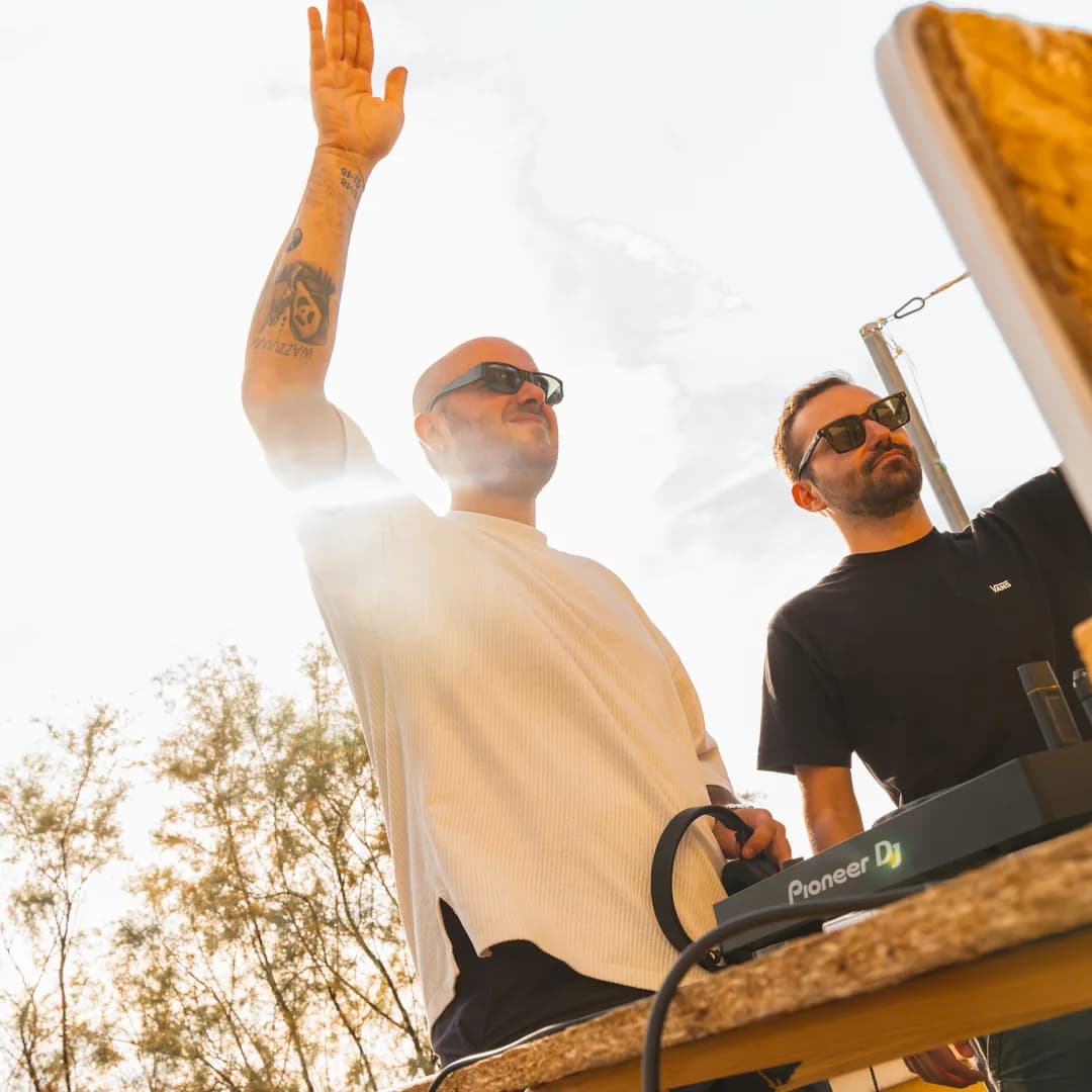 Due dj alla consolle in controluce, con il cielo dietro